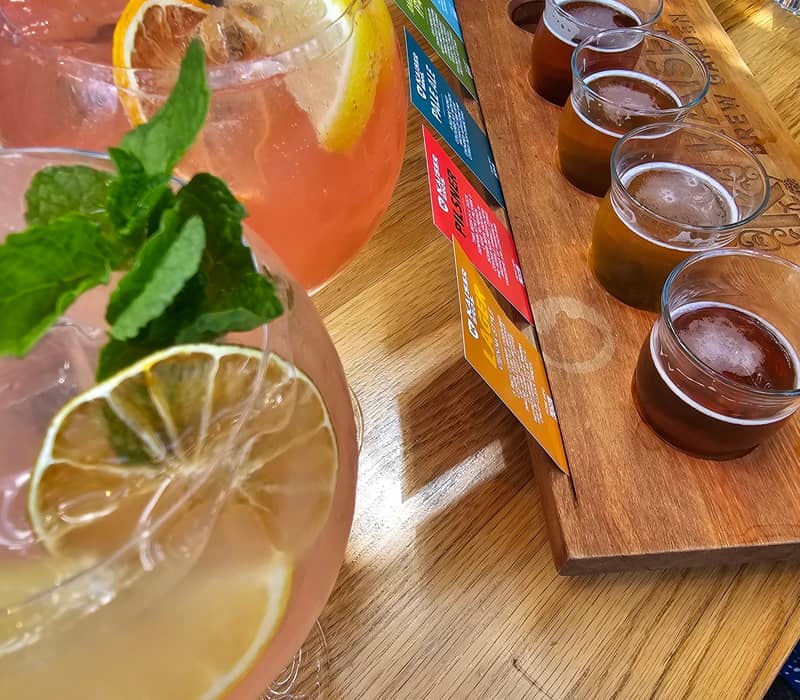 Two cocktails with lemon and mint garnishes and a wooden board holding five small beer glasses with a tasting menu. Credit: Amiki Tours