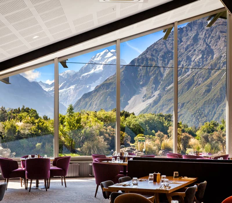 Indoor dining room with purple chairs and large windows showing alpine mountains and greenery outside. Credit: The Hermitage Hotel