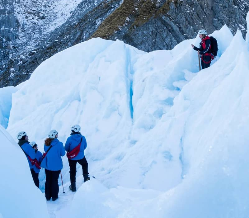 Group of people ice trekking with guide on Franz Josef Glacier snowy and icy terrain. Credit: Franz Josef Glacier Guides