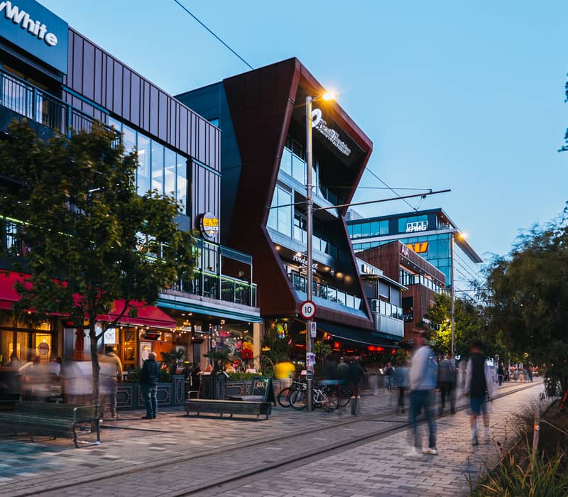 A busy street scene at dusk on Oxford Terrace in Christchurch, featuring glowing restaurants and modern architecture.