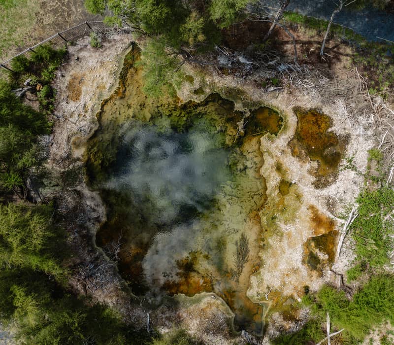 Aerial view of a colorful geothermal hot spring surrounded by green trees.