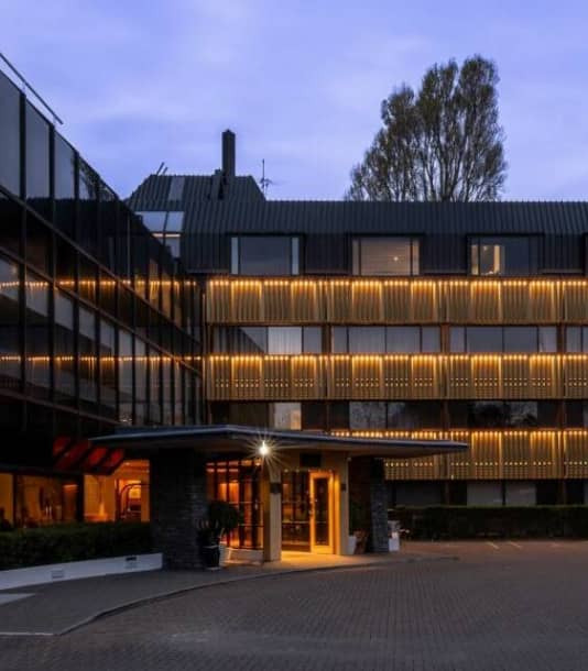 Modern hotel building with lit exterior and entrance at dusk Credit: The George Hotel - Christchurch