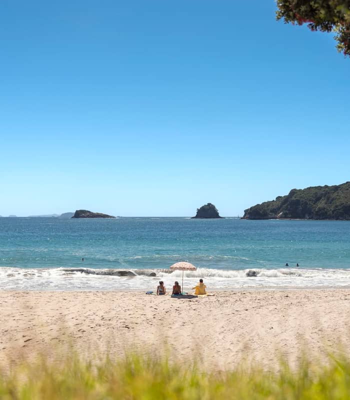 Couple relaxing on warm sand of Hahei Beach Coromandel.