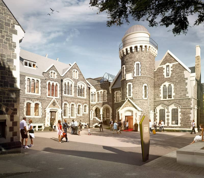 People walking and sitting outside the stone Observatory Hotel with a tower under a partly cloudy sky. Credit: The Observatory Hotel