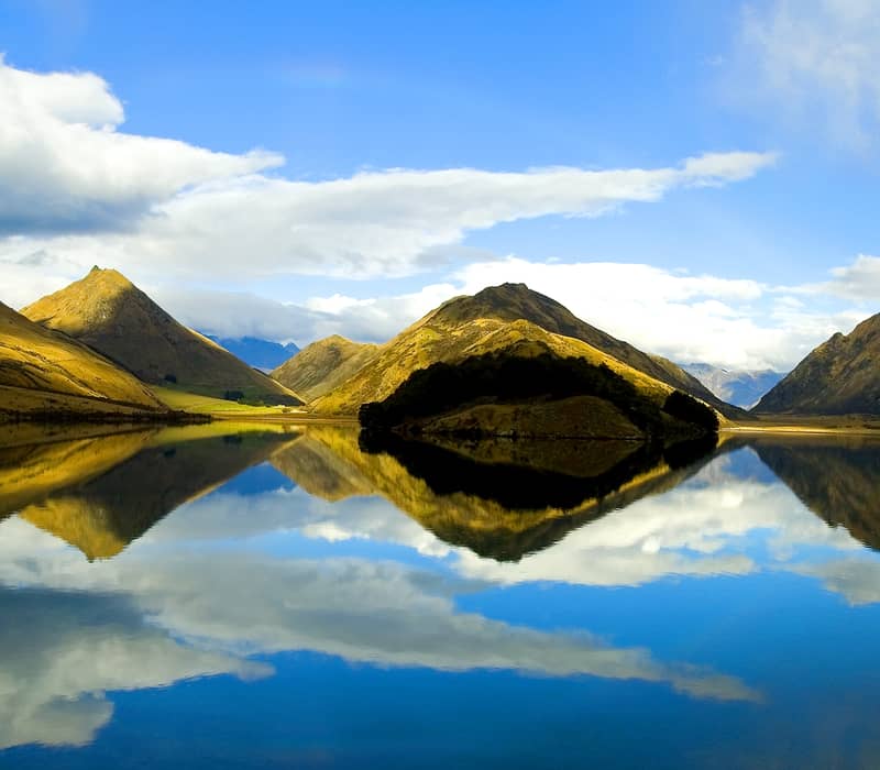 Calm lake reflecting mountains and clouds under blue sky