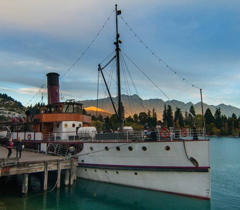 Steamship docked at a pier with mountains and water in the background during sunset.
