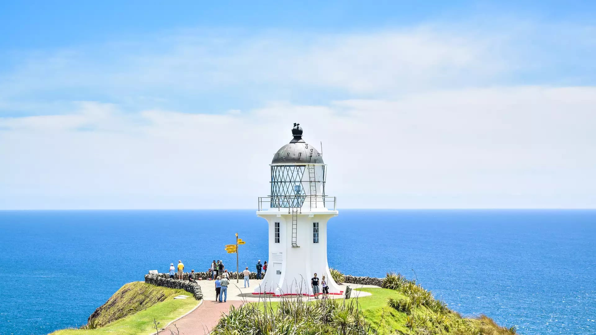 White lighthouse on cliff edge with people and vast blue ocean under a partly cloudy sky Credit: Fine Tours Group - Photographer unknown
