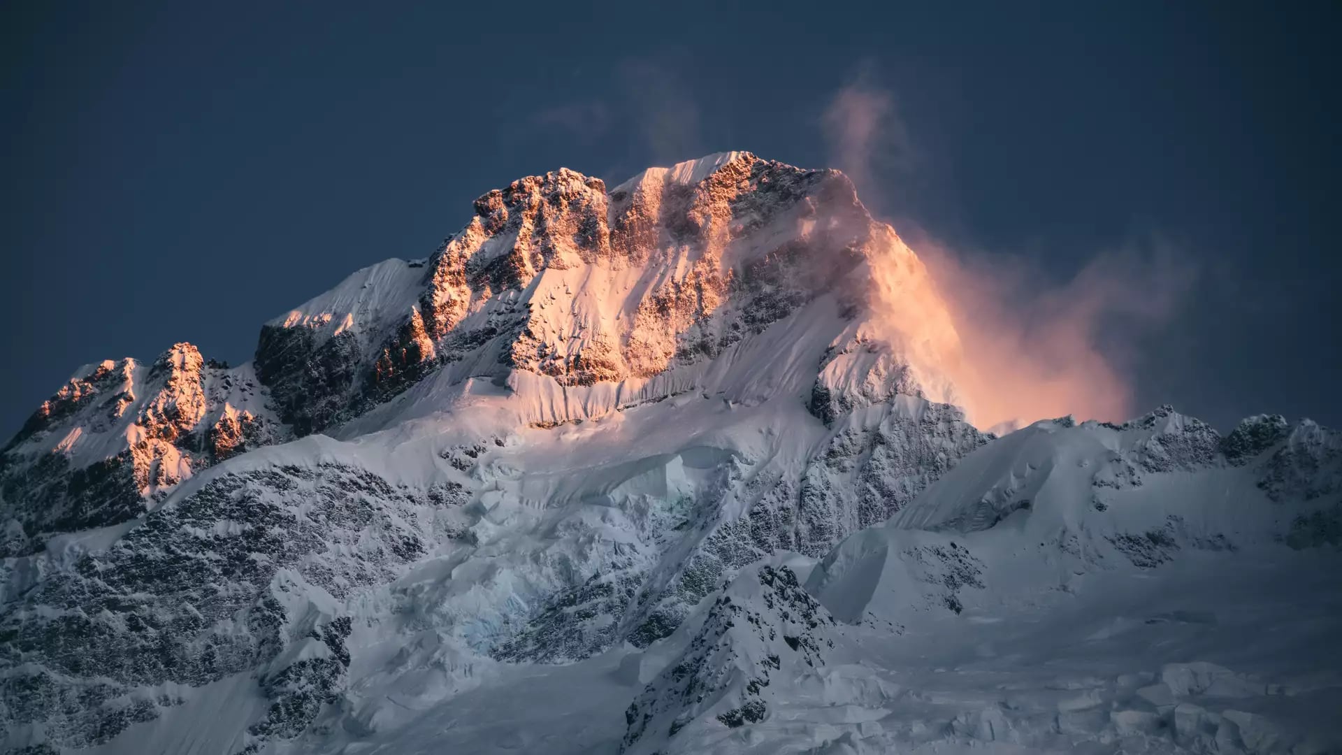 Snow-covered Mt Sefton glowing with orange sunset light against a dark blue sky.