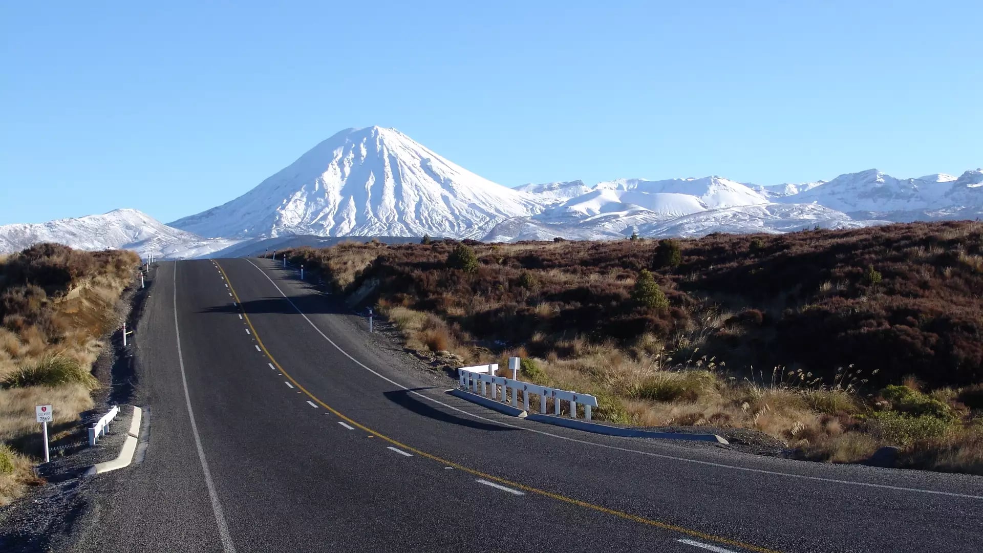 Paved road heading towards snow-covered Mount Ngauruhoe volcano under a clear blue sky. Credit: New Zealand Fine Touring