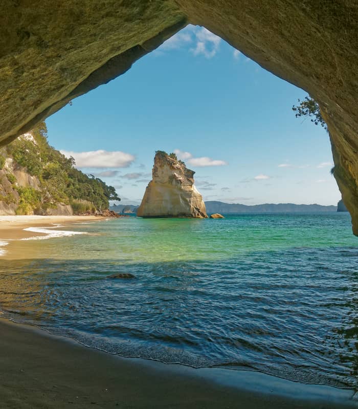 View of sandy beach and rock formation through a sea cave arch at Cathedral Cove.