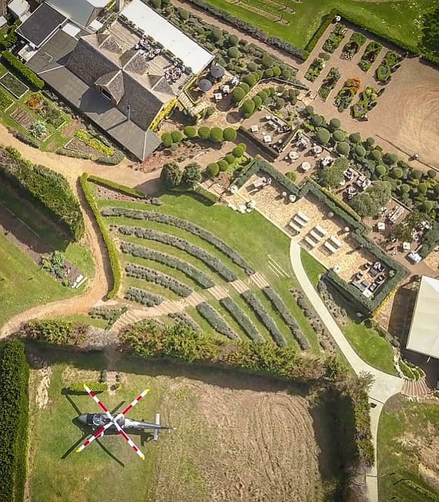 Helicopter landed on grass near vineyard gardens and outdoor dining tables at Mudbrick Vineyard.