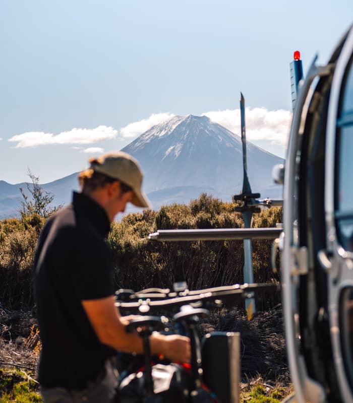 Man mounting Mountain bikes on helicopter with mountain in background.