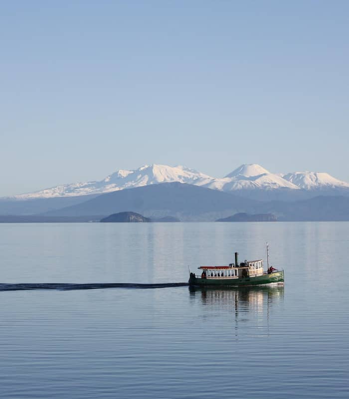 Boat cruising on Lake Taupo with snowy mountain in backdrop.