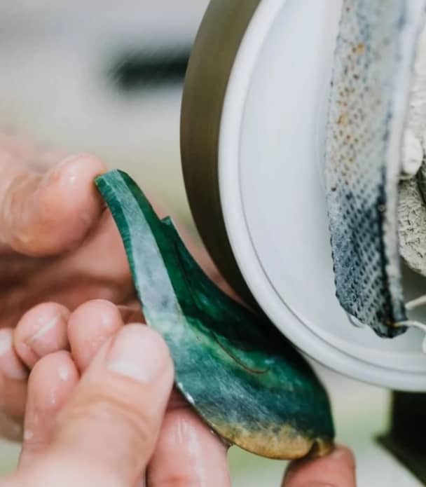 Hands polishing a green jade stone on a grinding wheel.