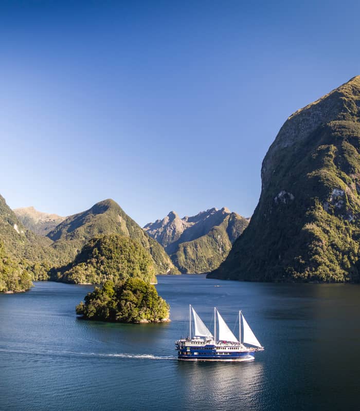 Cruise boat sailing in forested fjord with mountains and clear blue sky