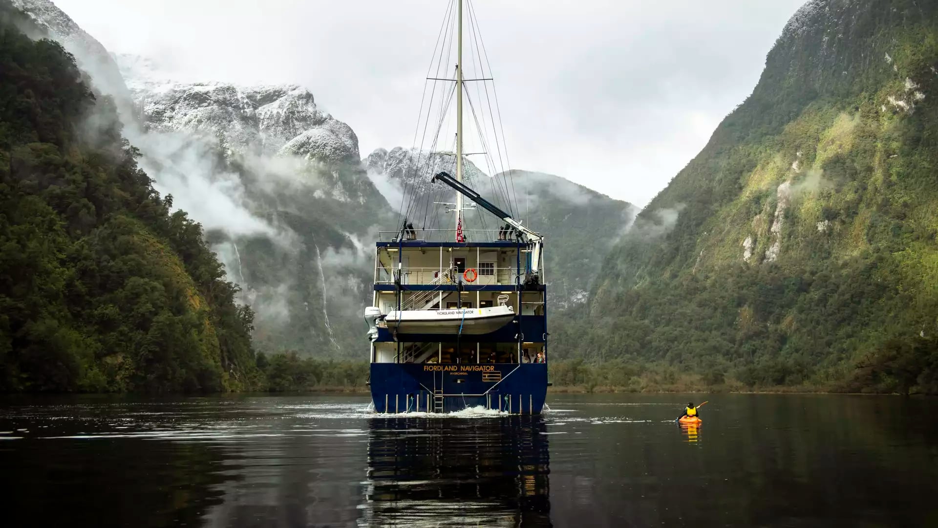 Cruise ship in fjord surrounded by foggy mountains and kayak on calm water