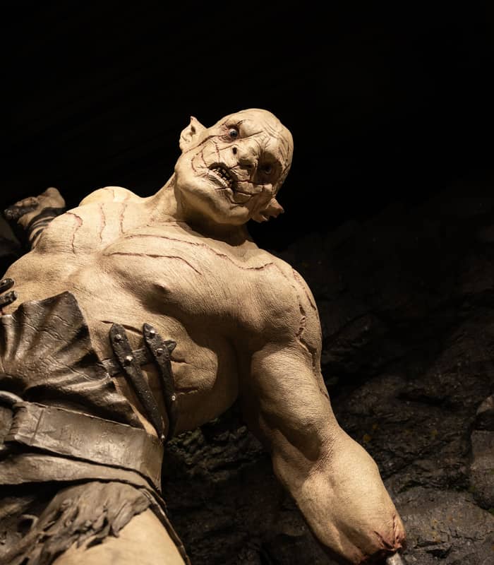 Muscular troll statue with scars and belt in a rocky cave environment.