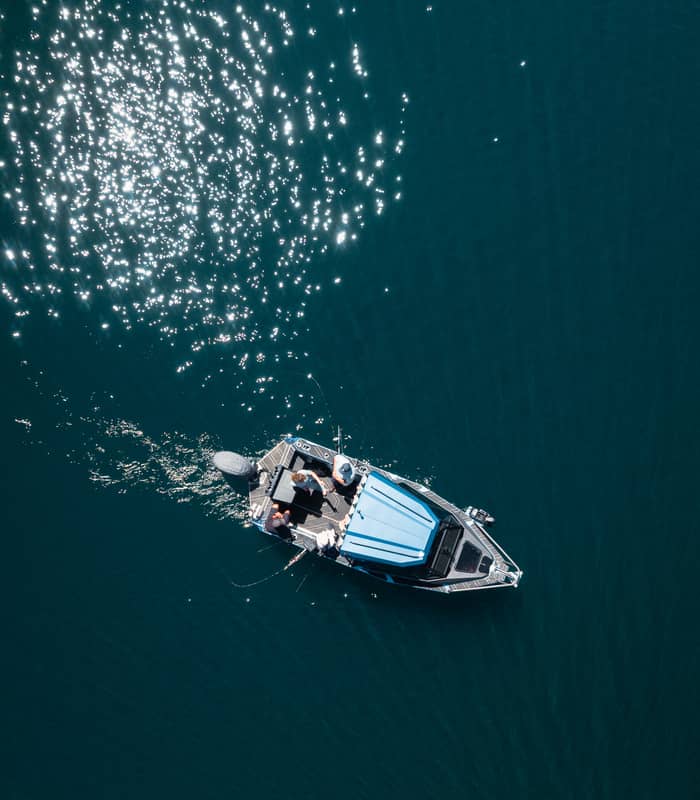 A fishing boat with three people on a shimmering blue lake under bright sunlight.