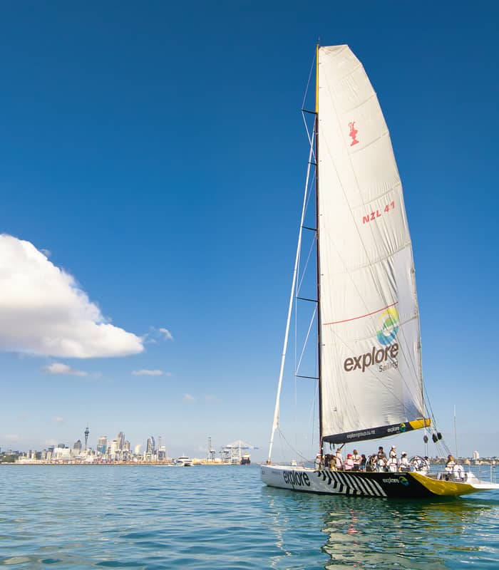 Sailboat with people sailing on water near a city skyline on a clear day.