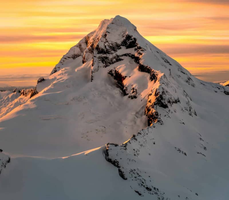 Snow-covered mountain peak glowing under golden sunset sky