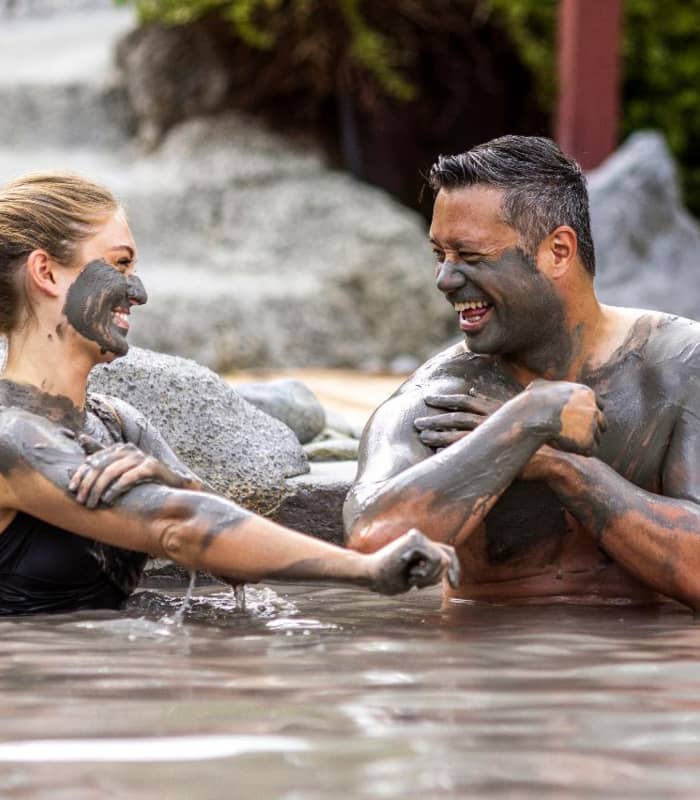 Happy couple covered in mud enjoying a mud bath outdoors, smiling and having fun.