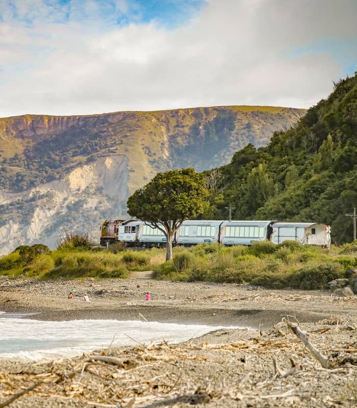 Train moving along beach coastline with mountains and ocean in the background.