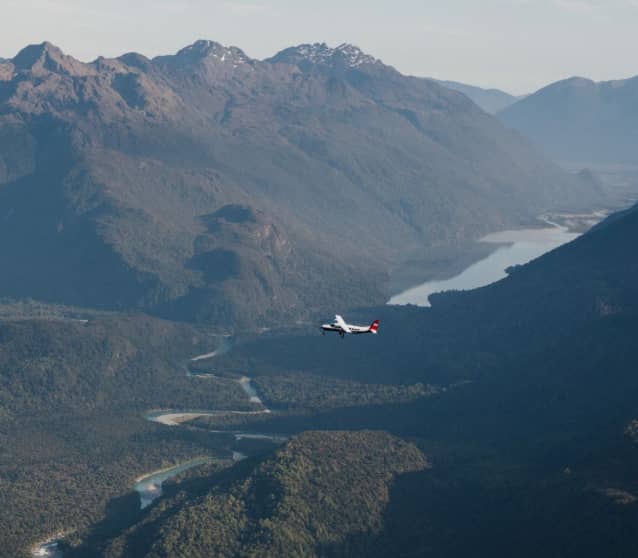 Small plane flying over green mountains and a winding river in Milford Sound. Credit: Milford Sound Scenic Flights