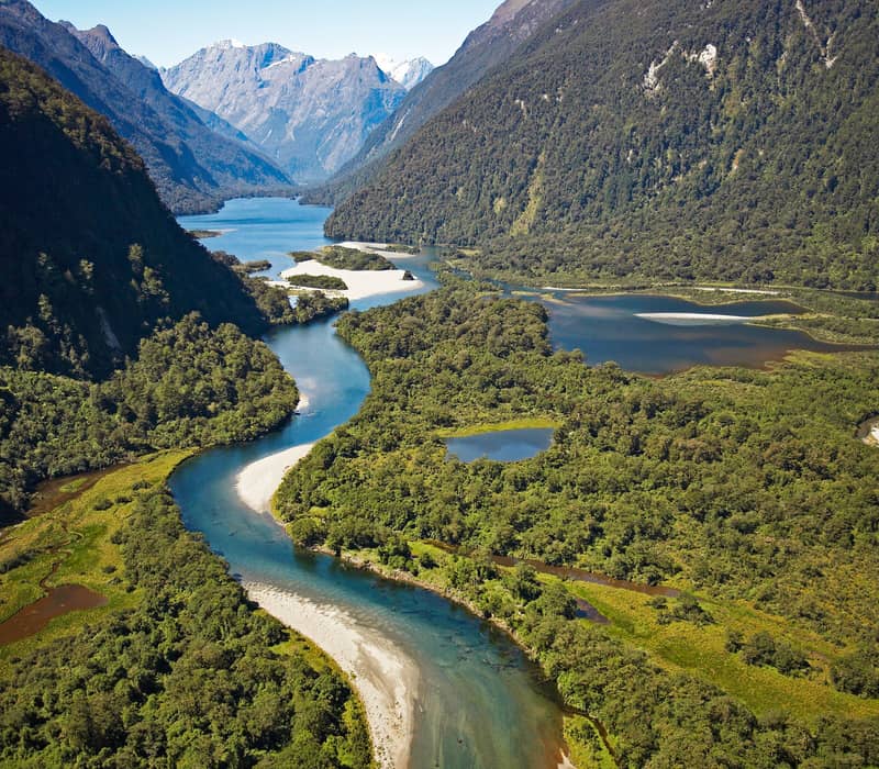 Winding river flowing through a green valley with mountains in the background.