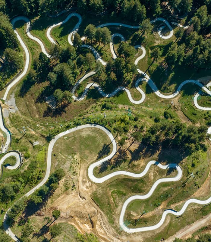 Aerial shot of winding luge tracks surrounded by forest and greenery on a hill.