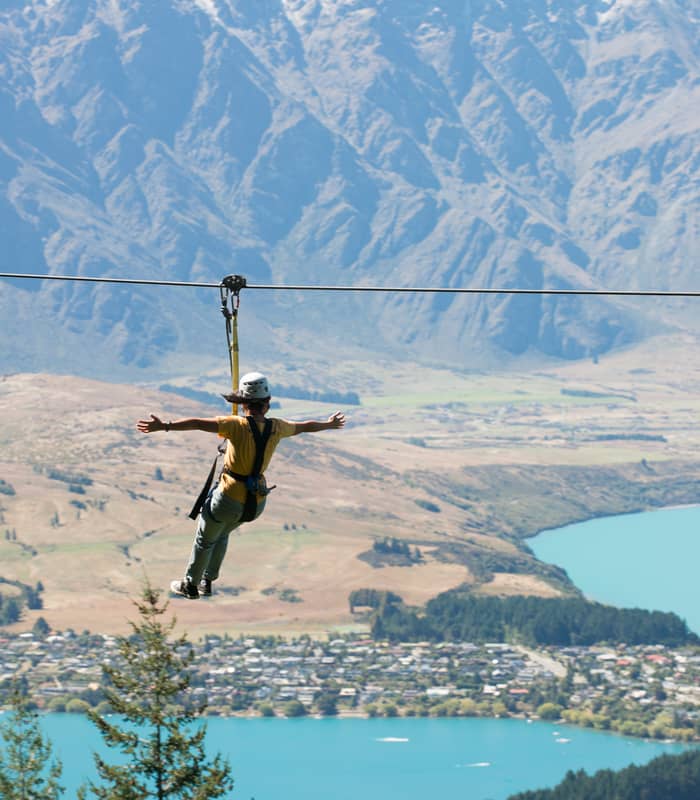 Person ziplining over a blue lake with mountains in the background.
